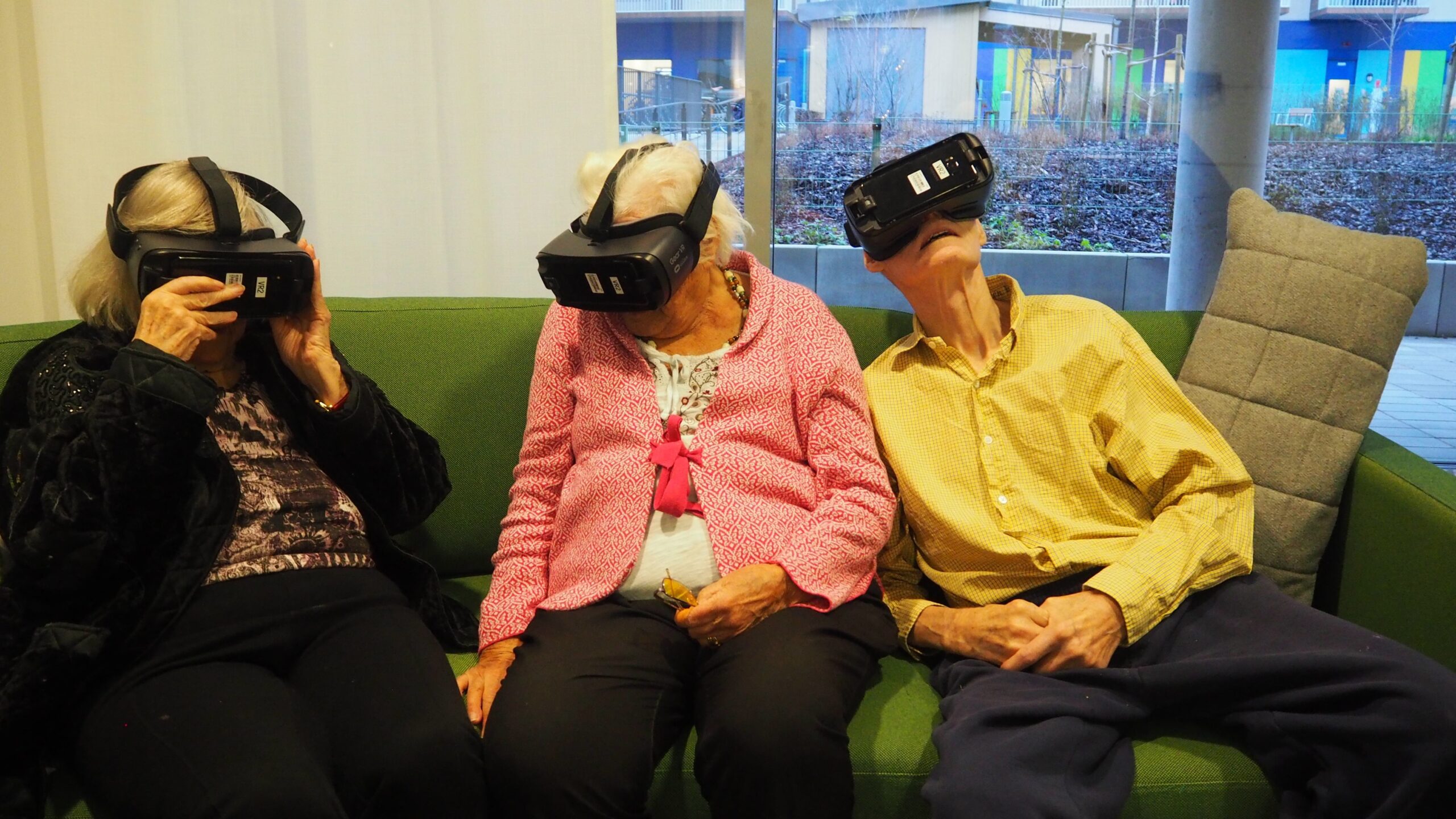Två kvinnliga och en manlig omsorgstagare sittandes i en soffa med VR-glasögon på sig