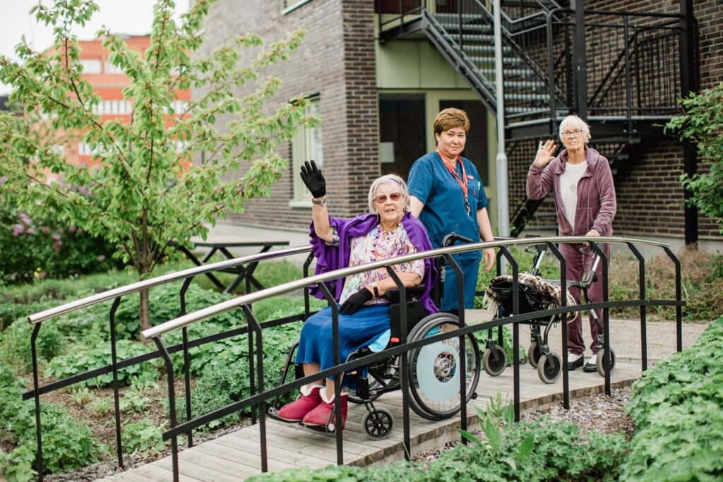 Två omsorgstagare i trädgården med en medarbetare