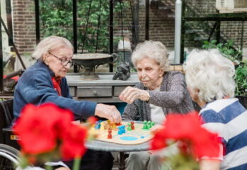 Tre äldre personer sitter i trädgården och spelar fia med knuff