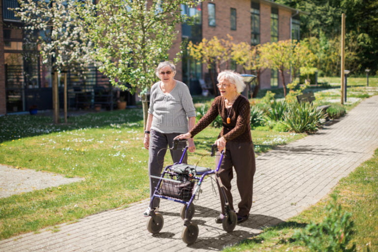Två boende promenerar i en grönskande trädgård