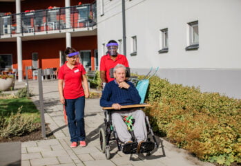 Två medarbetare promenerar tillsammans med boende i rullstol