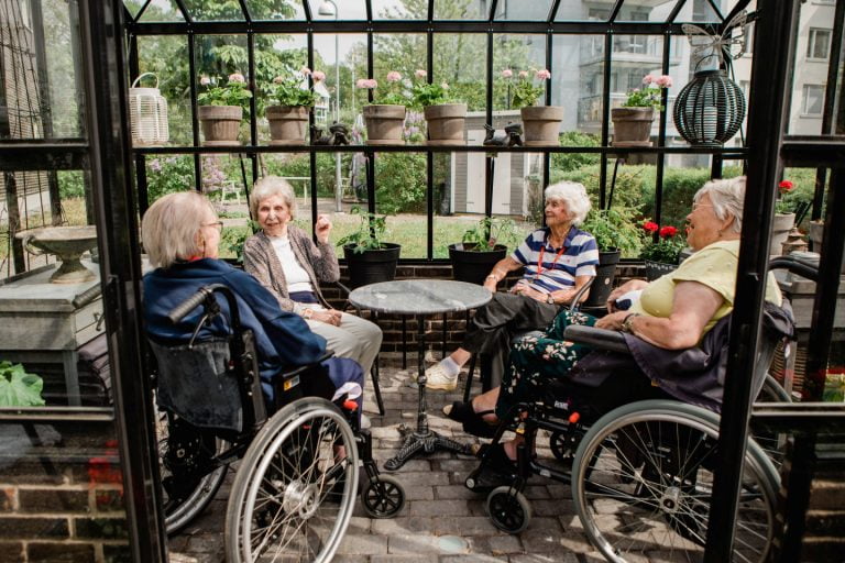 Fyra äldre personer sitter i ett växthus och samtalar