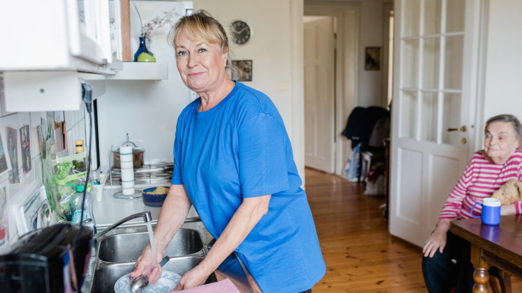 Medarbetare från hemtjänsten hjälper en kund att diska i hennes hem.