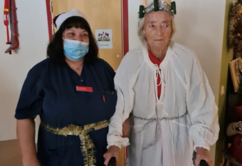 medarbetare i blått och munskydd äldre kvinna luciaklädd