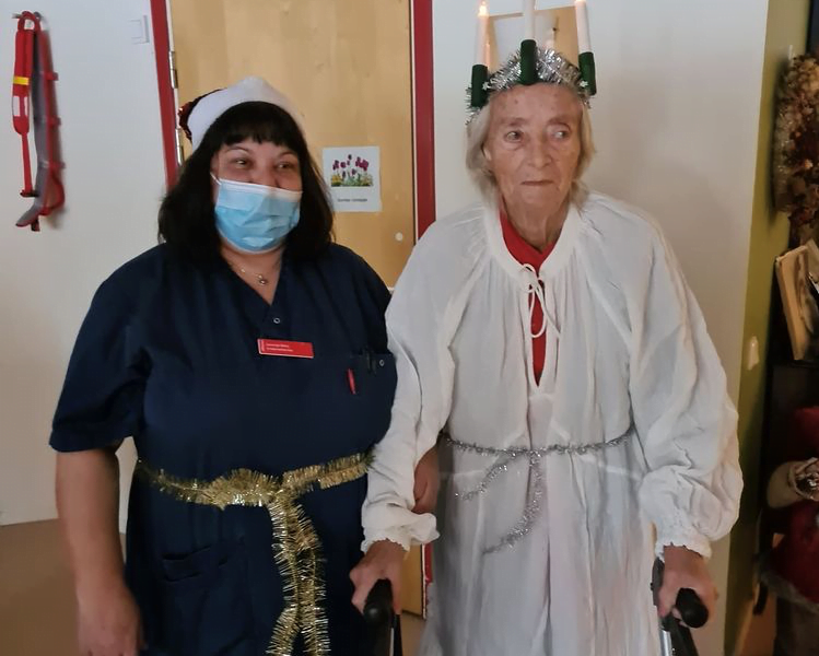medarbetare i blått och munskydd äldre kvinna luciaklädd