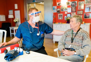 Sjuksköterska med munskydd och visir samtalar med en boende