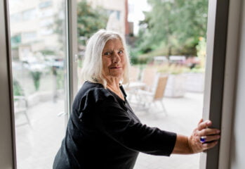En äldre person vänder sig mot kameran på väg genom dörren till en uteplats