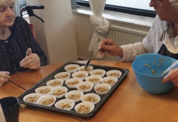 Två äldre personer lägger smet i formar på en bakplåt