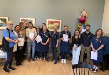 Gruppbild på medarbetare håller upp certifikat med ballonger i bakgrunden