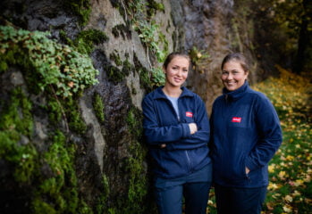 Två medarbetare står bredvid en mossbeklädd bergvägg