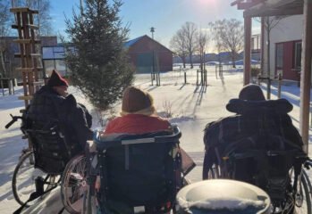 Ryggen på två boende i rullstol som tittar på solen i vintrigt landskap