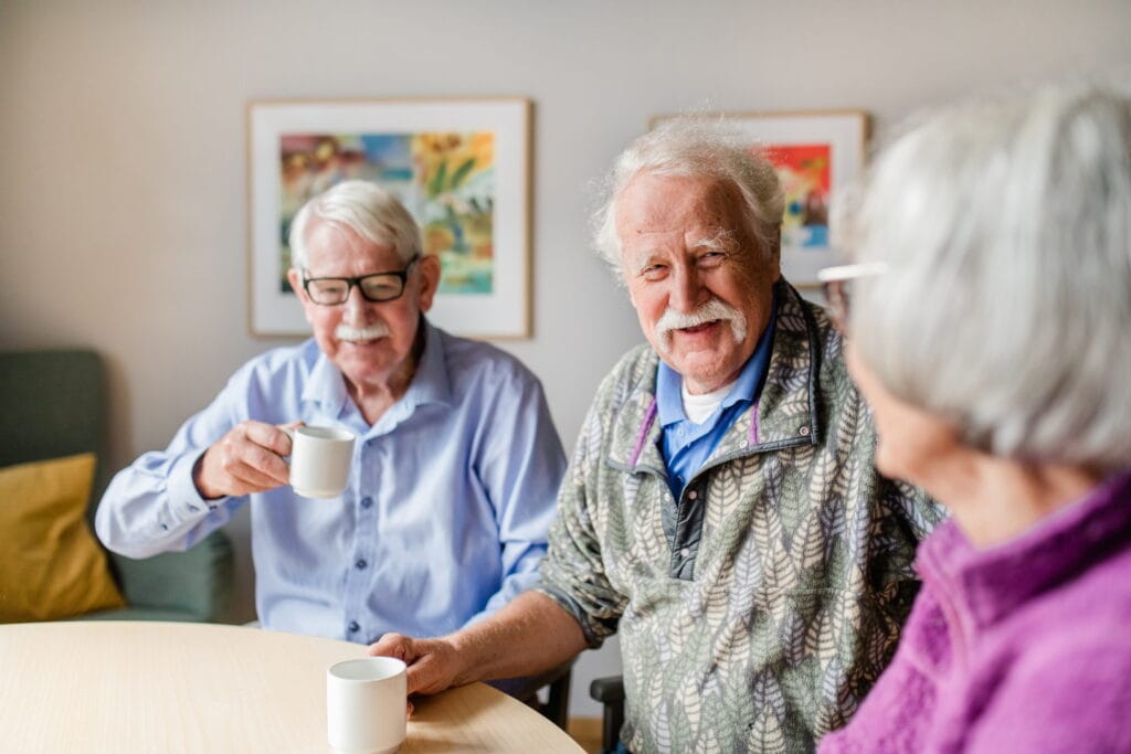 Tre boende dricker kaffe tillsammans. Tittar på varandra och ler.