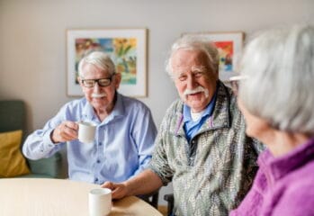 Tre boende dricker kaffe tillsammans. Tittar på varandra och ler.
