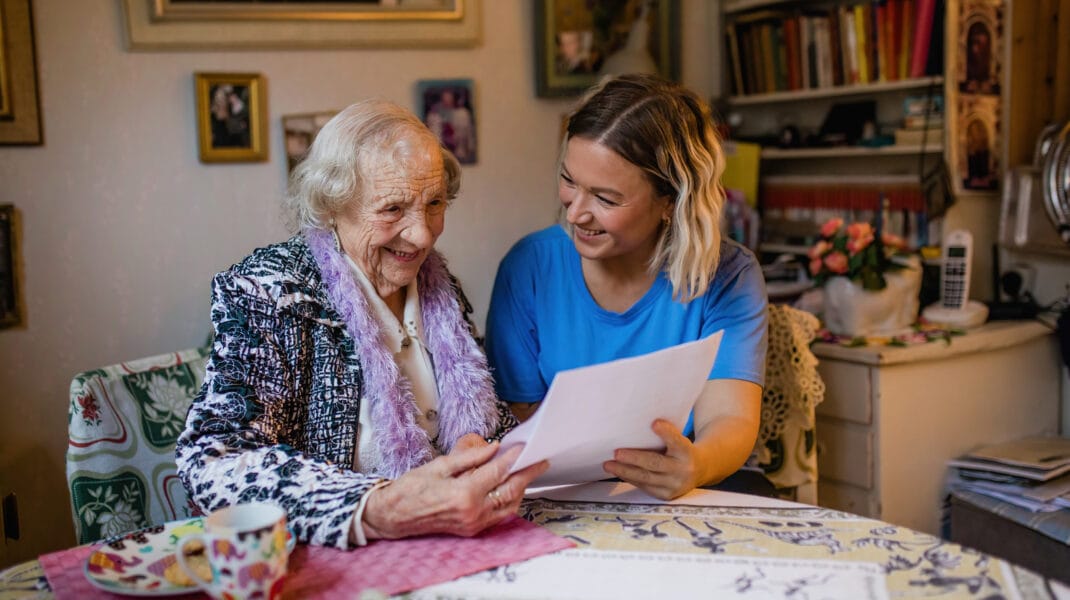 Äldre kvinna tittar på papper tillsammans med en personal