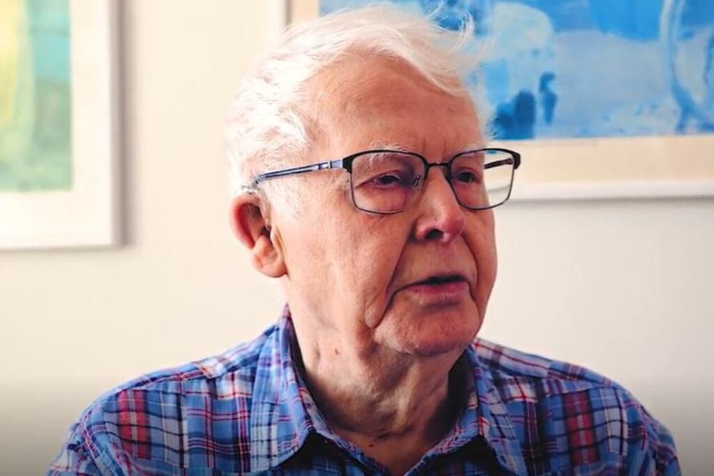 Porträttbild på Anders kort vitt hår, rutig skjorta och glasögon med svart båge