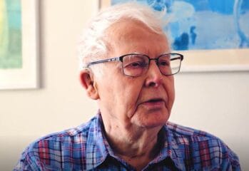 Porträttbild på Anders kort vitt hår, rutig skjorta och glasögon med svart båge