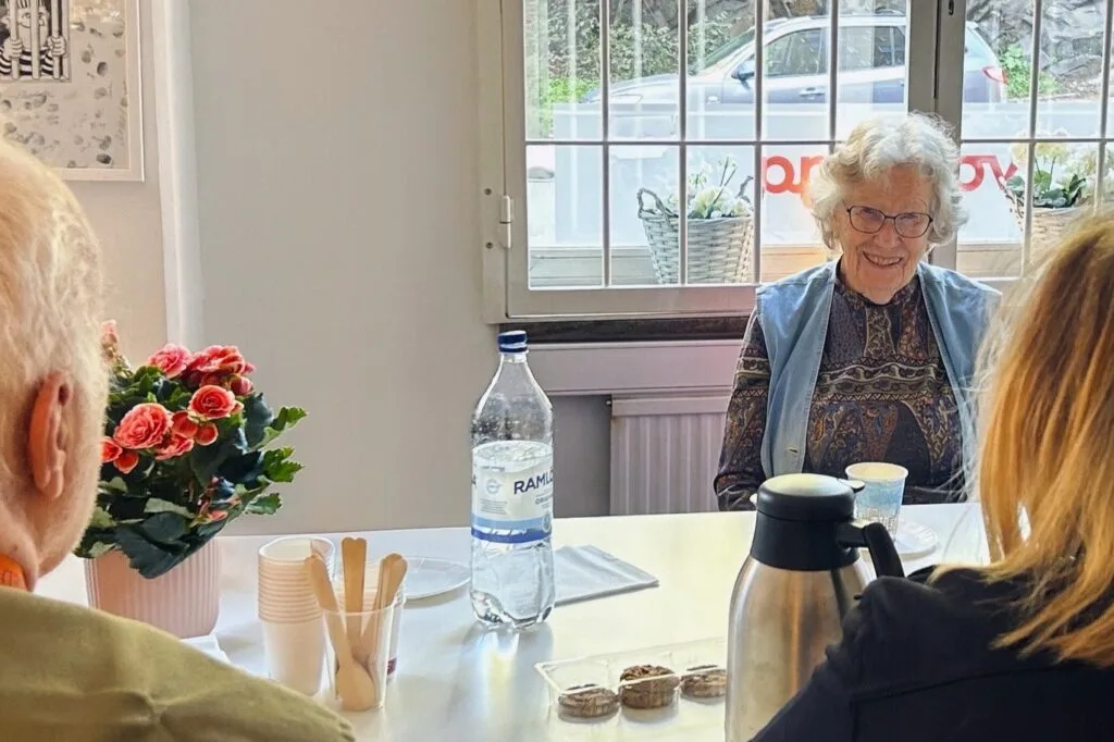 Kvinna sitter vid ett fikabord och ler tillsammans med andra