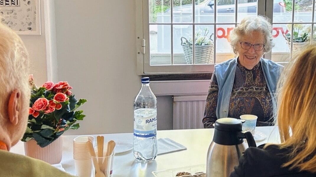 Kvinna sitter vid ett fikabord och ler tillsammans med andra