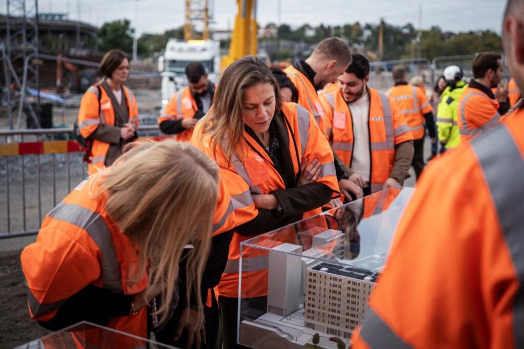 Deltagre i orange byggvästar tittar på minityr av byggprojekt i glasmonter.