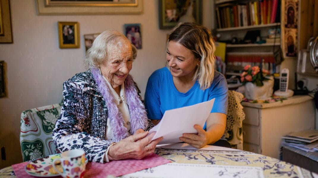 Äldre kvinna tittar på papper tillsammans med en personal