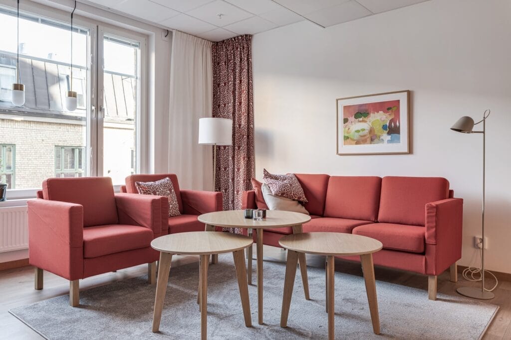 Ljust och hemtrevligt vardagsrum med rosa soffa och fåtölj, runda soffbord i trä, stora fönster och mjuka textilier.