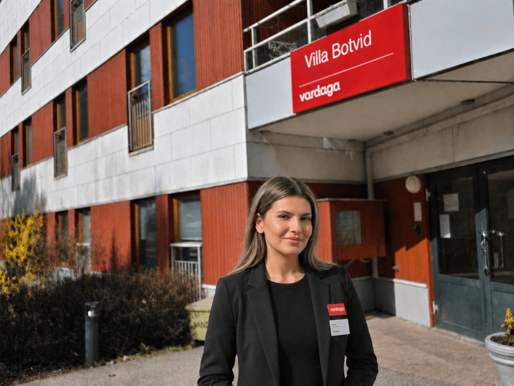 Kvinna i mörk kavaj står utanför äldreboendet Villa Botvid med Vardaga-skylt ovanför entrén.