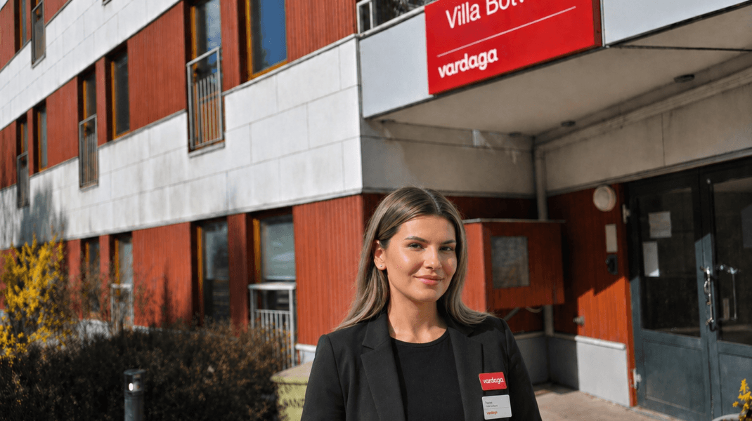 Kvinna i mörk kavaj står utanför äldreboendet Villa Botvid med Vardaga-skylt ovanför entrén.