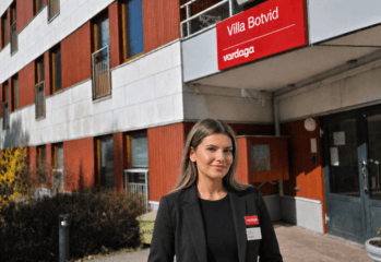 Kvinna i mörk kavaj står utanför äldreboendet Villa Botvid med Vardaga-skylt ovanför entrén.