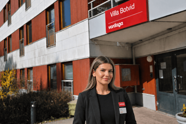 Kvinna i mörk kavaj står utanför äldreboendet Villa Botvid med Vardaga-skylt ovanför entrén.